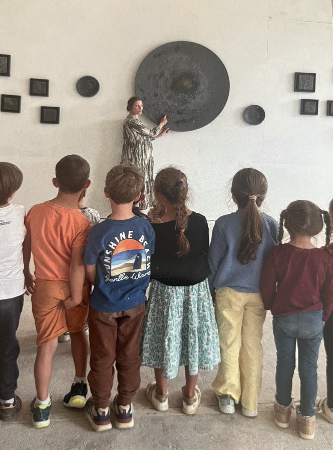 Une artiste présente une grande œuvre circulaire à une classe d'écoliers réunis devant elle