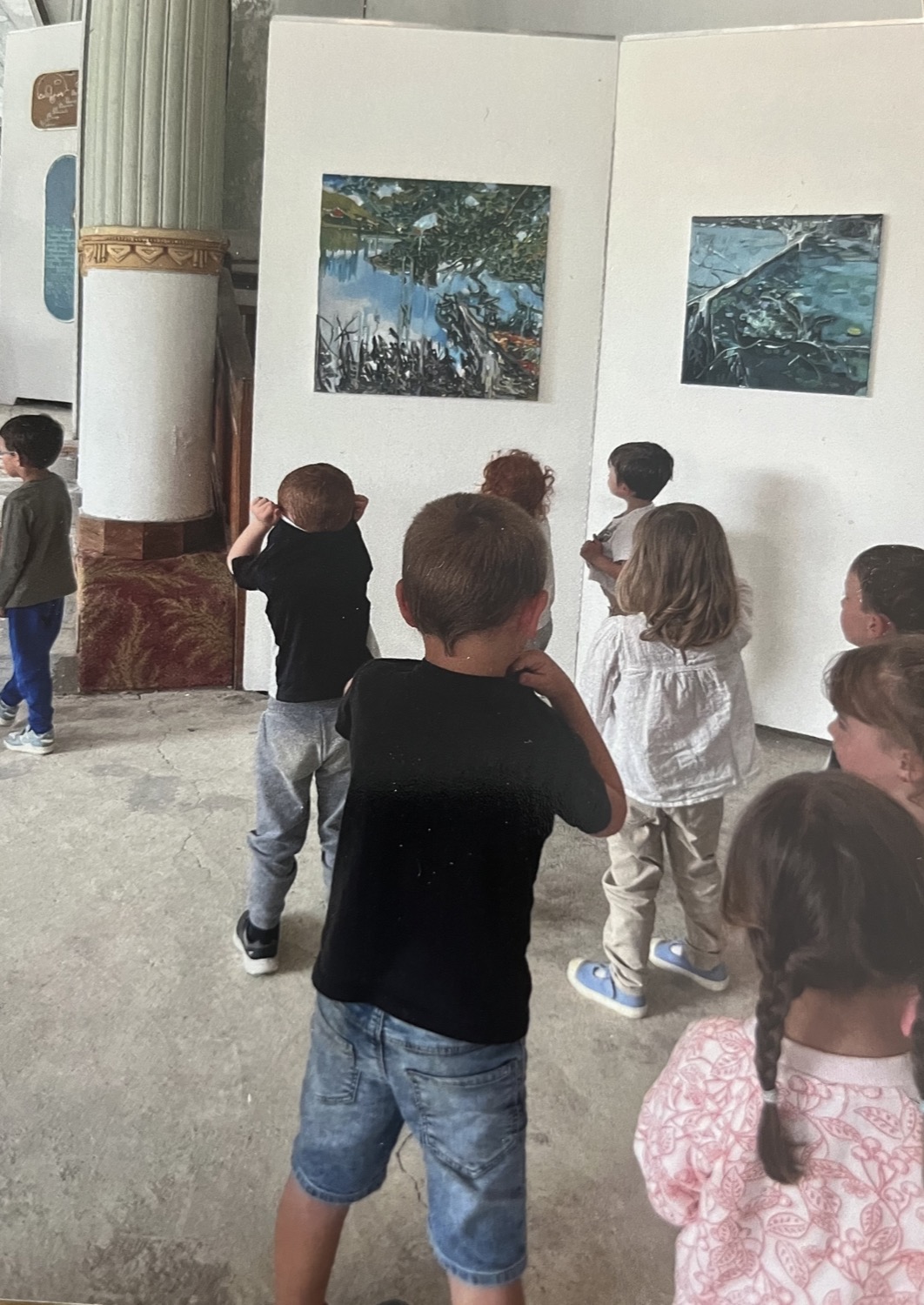 De jeunes écoliers observent des tableaux accrochés sur les cimaises de l'exposition
